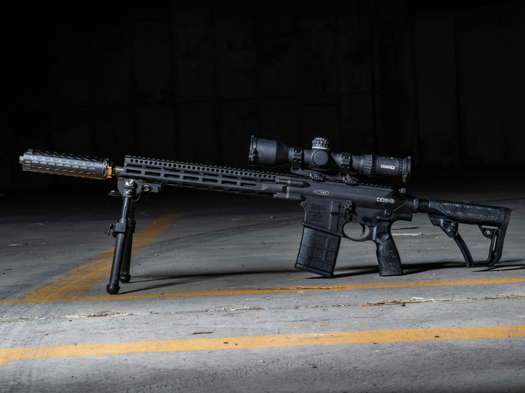 Rifles with scope and bipod on a concrete floor with a dark background